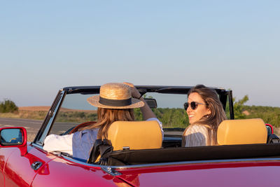 Side view of beautiful young women talking, smiling and having fun driving on a red convertible car