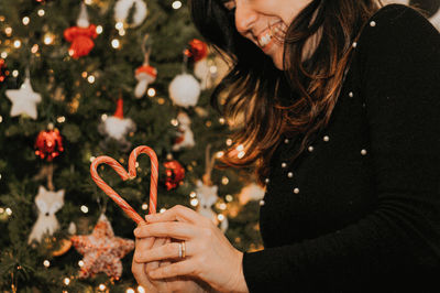 Midsection of woman holding candy cane against christmas tree