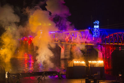 Smoke over river by illuminated bridge during festival at night