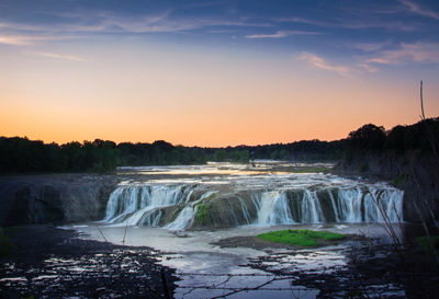 Scenic view of waterfall against sky during sunset