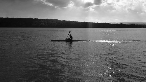 Silhouette man sculling in lake against sky