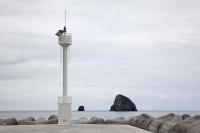 Beacon on pier amidst tetrapod in sea against sky