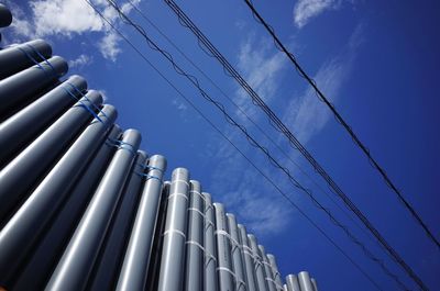 Low angle view of pipes and power lines against blue sky