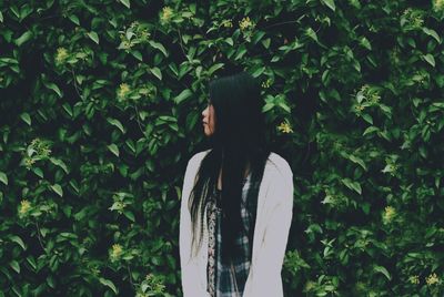 Young woman standing against plants