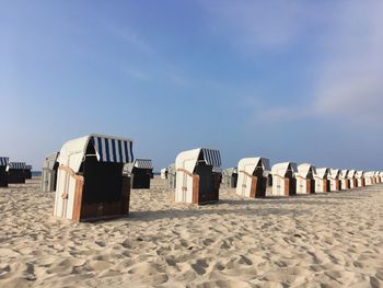 Hooded beach chairs on sand against sky