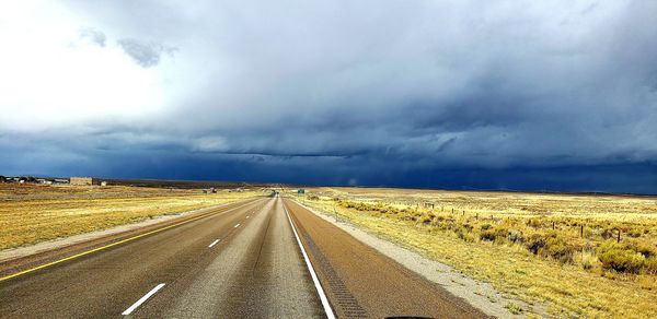 View of road along landscape against cloudy sky