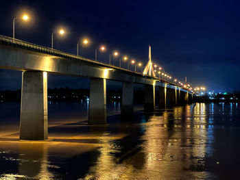 Illuminated bridge over river against sky at night