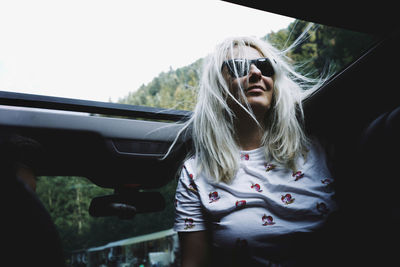 Low angle view of woman wearing sunglasses in car at sun roof