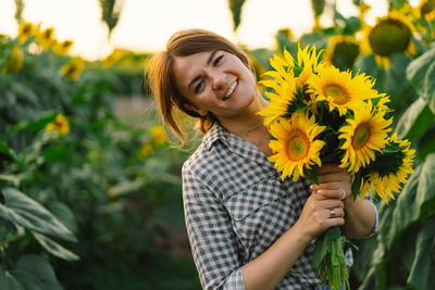 Beautiful young woman with sunflowers enjoying nature and laughing on summer sunflower field.