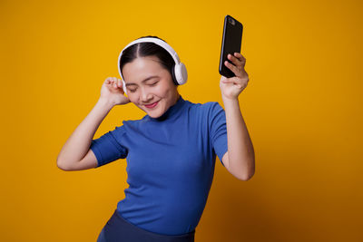 Young woman using mobile phone against yellow background