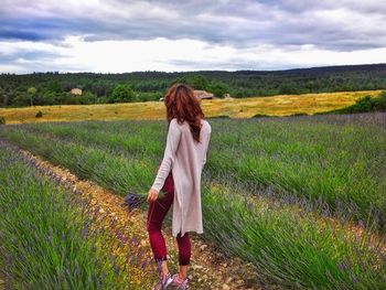 Rear view of woman walking on field against sky