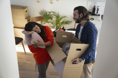 Woman leaning on pillow while man carrying box in new house