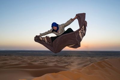 Full length of young woman jumping on beach against clear sky