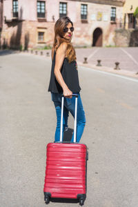 Mature woman pulling suitcase while walking on road in city during sunny day