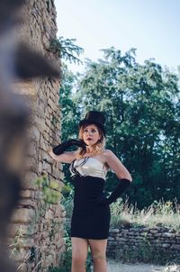 Young woman standing by brick wall in park