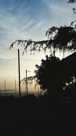 Silhouette fence and trees on field against sky at sunset