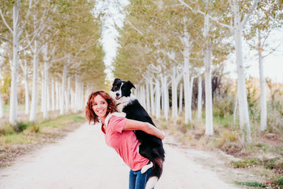 Smiling woman carrying dog while standing in forest