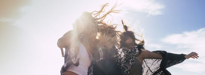 Happy female friends dancing against sky