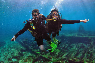 A man and a woman couple doing scuba diving near a shipwreck