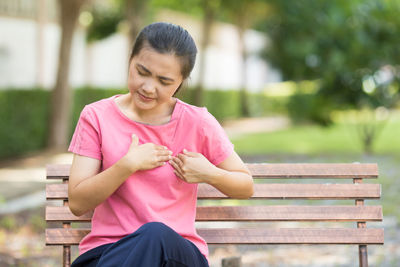 Young woman suffering from chest pain while sitting on bench at park