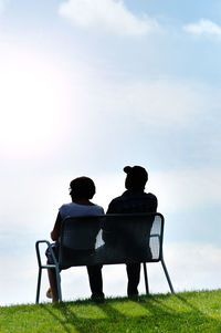 Rear view of couple sitting on bench against sky