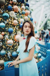 Smiling young woman looking away while standing by christmas tree outdoors