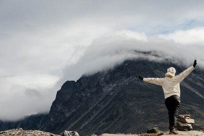 Rear view of woman standing on rock against sky