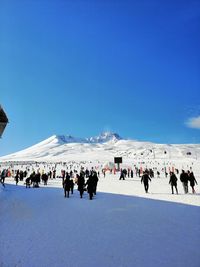 People on snow covered mountain against blue sky