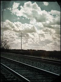 Railroad tracks against cloudy sky