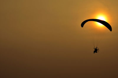 Silhouette person paragliding against sky during sunset