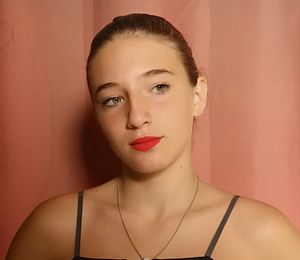 Girl wearing red lipstick while looking away against wall
