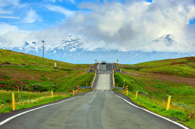 Down the road to the bridge there was a car coming, panoramic view of rural view in iceland.