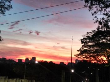 Silhouette trees and buildings against dramatic sky