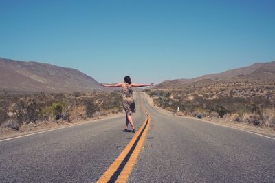 Woman walking on country road against clear sky