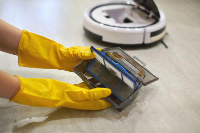 Dust storage box case of robotic vacuum cleaner in gloved female hands. taking out filter to clean