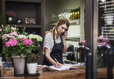 Florist writing in note pad while talking on mobile phone