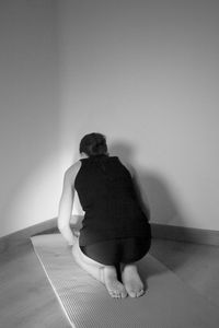 Rear view of woman sitting on hardwood floor against wall