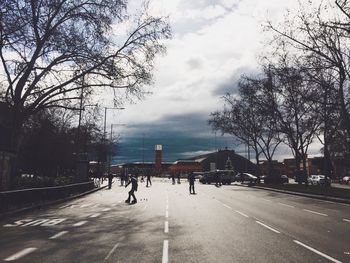 Road by bare trees against sky in city