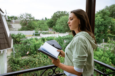 Young woman stands on the balcony with notepad in hand