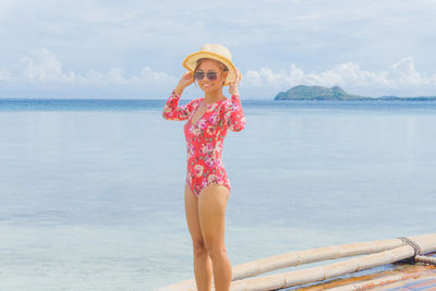 Smiling woman in swimsuit standing on raft by sea against sky