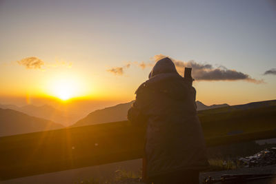 Rear view of woman looking at sea against sky during sunset