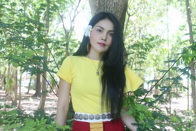 Portrait of beautiful young woman standing against trees