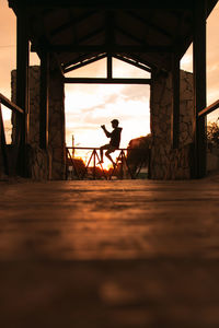 Silhouette man standing on railroad track against sky during sunset