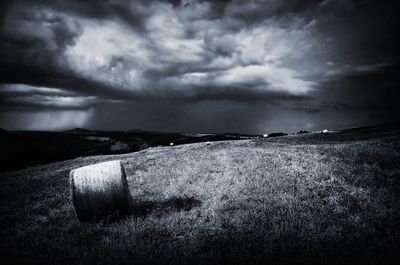 Hay bales on field against storm clouds