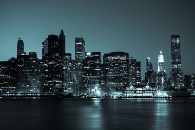 Illuminated buildings by river against sky in city at night