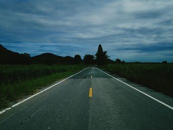 Diminishing perspective of empty road amidst landscape against cloudy sky at dusk