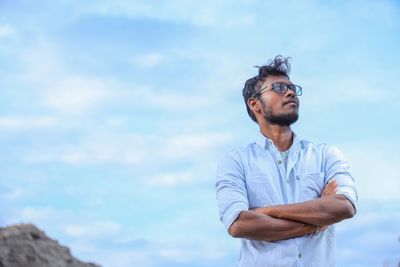 Young man looking away while standing against sky