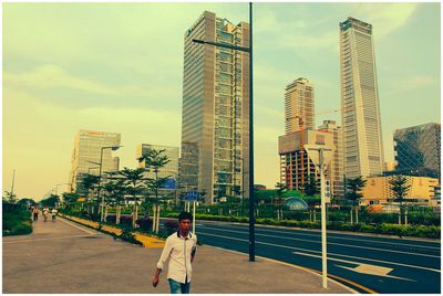 Rear view of man walking on street by buildings against sky