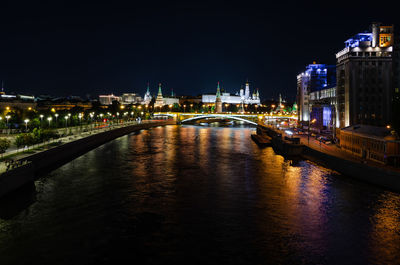 Illuminated bridge over river by buildings against sky at night