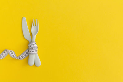 Measuring tape and cutlery on yellow background. weight loss concept